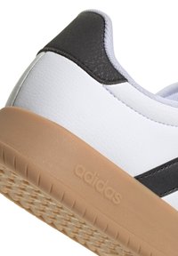 Baskets blanches avec accents noirs, dessus en cuir texturé et semelle en caoutchouc beige avec motif de grip texturé et logo embossé.