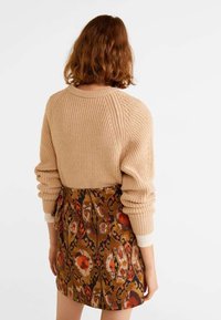 Beige neulepaita, jossa on raglan-hihat, yhdistettynä kuvioituun ruskeaan hameeseen, jossa on kukkakuoseja punaisen ja oranðin sävyissä.