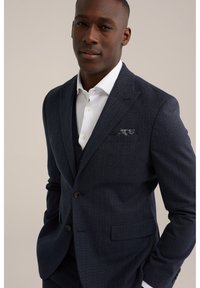 Costume bleu marine en chevrons avec revers à cran, fermeture à un bouton et une texture subtile. Comprend une chemise blanche et un mouchoir de poche à motif.