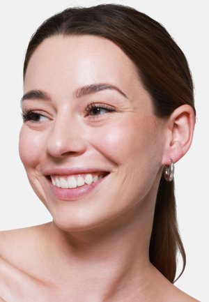 Orecchino a cerchio in argento indossato da una donna sorridente con un tono di pelle medio. L'orecchino presenta una superficie liscia e lucida e una forma circolare.
