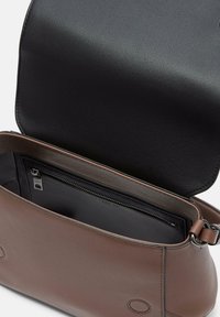 Bolso de mano de cuero marrón con una solapa negra brillante, que presenta un acabado texturizado y un bolsillo con cremallera en el interior. Diseño minimalista con acentos metálicos.