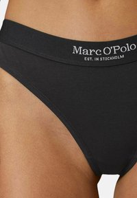 Culottes en coton noir avec une large ceinture élastique arborant le logo blanc "Marc O'Polo" et un design épuré pour le confort et le maintien.
