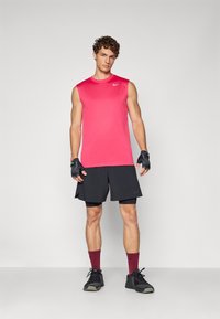 Strój sportowy składający się z bezrękawnika w kolorze różowym marki Nike, czarnych szortów i czarnych sneakersów, z bordowymi skarpetkami i czarnymi rękawiczkami.