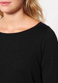 Schwarzes Strickoberteil mit weitem Ausschnitt und kurzen Ärmeln, ausgestattet mit einem strukturierten Stoff und sichtbaren Nähten.