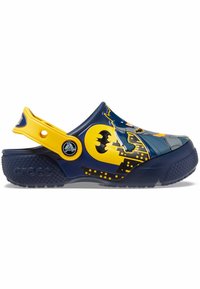 Des Crocs bleus et jaunes avec un design Batman, comportant une semelle texturée, une sangle latérale et des accents de paysage urbain. Matériau léger et durable.