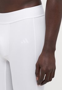 Hvide atletiske leggings med en glat, strækbar tekstur, der har en bred talje og subtil hvid branding på siden.