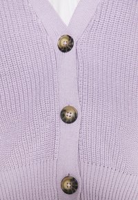 Lavendelstickad kofta med V-hals, prydd med fyra stora runda knappar i en mörk nyans och kontrasterande ljusare knappdetaljer.