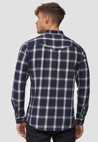 Navy and white plaid flannel shirt with long sleeves, featuring a pointed collar, button cuffs, and a curved hem design.