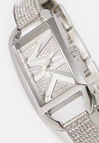 Reloj de pulsera rectangular plateado con esfera geométrica adornada con cristales y pulsera metálica a juego incrustada con cristales.