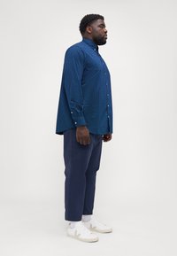 Blå knapp-up skjorta med vitt prickmönster, långa ärmar och krage, kombinerad med marinblå byxor och vita sneakers.