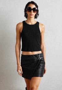 Top court noir à côtes associé à une jupe-culotte en cuir noir avec un design asymétrique et des accents en boucle métallique.