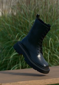 Black leather ankle boot with a rounded toe, lace-up front, and chunky rubber sole. Smooth finish with textured accents and pull tab.