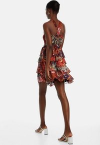 Robe mini à imprimé floral avec volants superposés, dotée de bretelles réglables et d'un motif coloré dans des tons de rouge, bleu et or.
