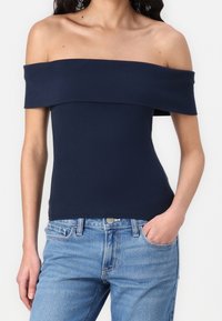 Top navy a spalle scoperte con texture a coste, design aderente e scollatura ampia, abbinato a jeans in denim blu chiaro.