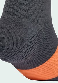 Melna zeķe ar ribotu tekstūru un oranžu joslu. Piedāvā ciešu pieguli pie potītes, uzsverot izturīgas šuves un austu materiālu.