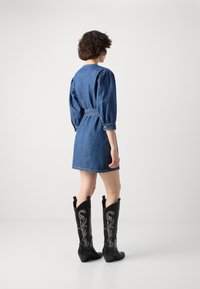 Denimkjole med puffede ærmer og bælter i taljen, parret med knæhøje sorte cowboystøvler med sølvbroderede designs.
