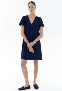 Navyblaues Kurzarmkleid mit V-Ausschnitt, lockerer Passform und glattem Stoff. Kombiniert mit dunklen Slippern. Minimalistisches Design, ohne Muster oder Akzente.