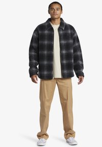 Black and gray plaid jacket with a collared neck, soft texture, zip closure, paired with beige chinos and white sneakers.