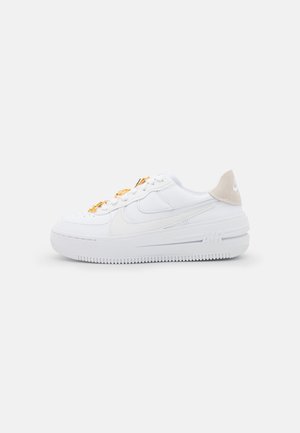 Biały niski sneaker z beżową zakładką na pięcie, złotymi ozdobami na sznurowadłach oraz grubą teksturowaną podeszwą na jednolitym tle, widok boczny na prawo.