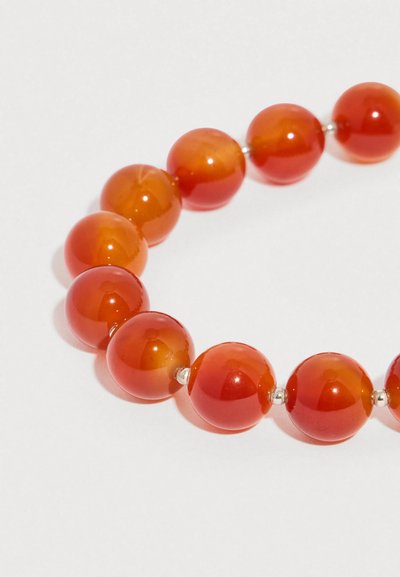 Γυαλιστερές στρογγυλές κόκκινες πορτοκαλί χάντρες περασμένες σε σειρά με μικρά ασημένια διαχωριστικά πάνω σε ανοιχτό φόντο, σχηματίζοντας έναν μερικό κύκλο.