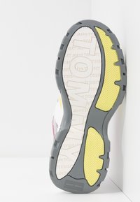 Podešev tenisků s šedou gumovou základnou a texturovanými žlutými akcenty, s viditelným brandingem v světlé barvě na podrážce.