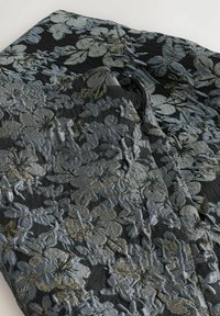 Sort stof med sølv- og guldblomster jacquard mønster, der viser en delvist åben sort lynlås og en sort knap.