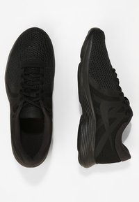 Musta urheilukengät, joissa on verkkomateriaali, teksturoituja yksityiskohtia ja uritettu pohja. Nauhat ovat punottu silmukoiden läpi varmistaen turvallisen kiinnityksen.