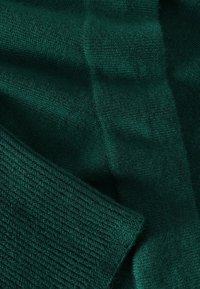 Grüner Strickstoff mit unterschiedlichen Texturen; zeigt ein glattes und geripptes Muster, das eine reiche Farbtiefe darstellt. Weich und leicht im Aussehen.