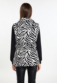 Czarna i biała kamizelka puchowa w zebra z wcięciem w talii, z kołnierzem i gładką, wyściełaną teksturą. Noszona na czarnej bluzce z długim rękawem.