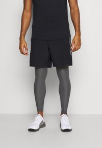 Des shorts de sport noirs associés à des leggings gris et des baskets blanches. Les shorts ont une coupe décontractée et un panneau en mesh sur le côté pour une meilleure respirabilité.