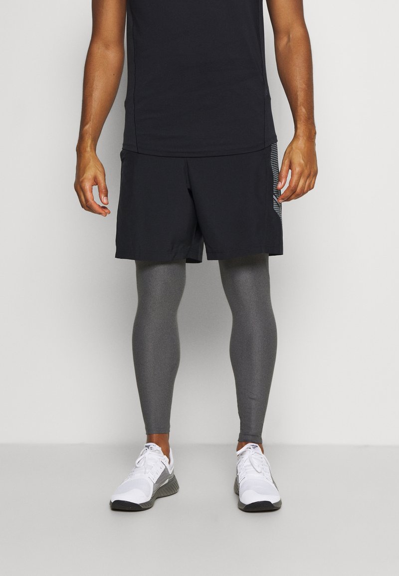 Des shorts de sport noirs associés à des leggings gris et des baskets blanches. Les shorts ont une coupe décontractée et un panneau en mesh sur le côté pour une meilleure respirabilité.