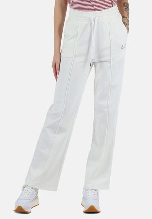 Pantaloni della tuta bianchi con vita regolabile tramite cordoncino, dotati di tasche laterali, dettagli di cucitura e vestibilità rilassata. Indossati con sneakers bianche.