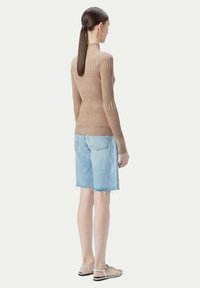 Beige ribbad tröja med långa ärmar, kombinerad med ljusblå denimshorts med trasiga kanter, och platta sandaler. Bakifrån.