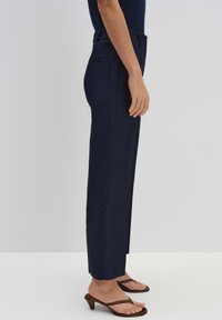 Pantalons bleu marine, fuselés, en tissu texturé avec poches latérales et taille mi-haute, associés à des sandales brunes à enfiler.