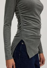 Grijze long sleeve top met getextureerde rimpeling aan de zijkanten, met een high-low hem en een zijsplit, gecombineerd met donkere denim.
