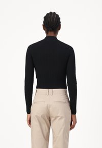 Melna ribota adīta džemperis ar augstu apkakli, pieguļošu dizainu un garām piedurknēm, saskaņots ar pelēkām biksēm ar aizmugurējām kabatām.