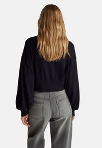 Černý zkrácený svetr s balónovými rukávy kombinovaný s kalhotami z lehkého šedého denimu s vysokým pasem. Látka vypadá měkce s texturovaným povrchem.