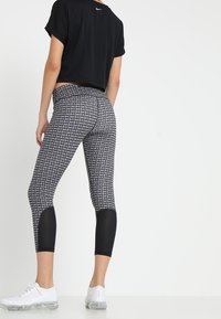 Czarny crop top o perforowanej fakturze, w połączeniu z wzorzystymi legginsami w czarno-białe wzory, posiadającymi siateczkowe akcenty i skróconą długość.
