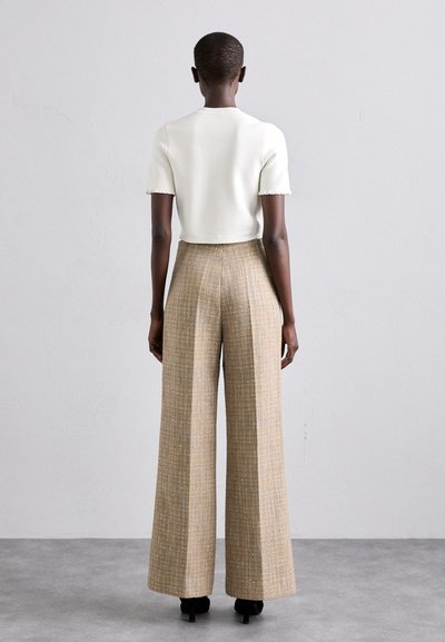 Hvid cropped t-shirt med bølgede ærmer, parret med beige, vidde bukser i tekstureret materiale med lodrette linjer og subtil glans.