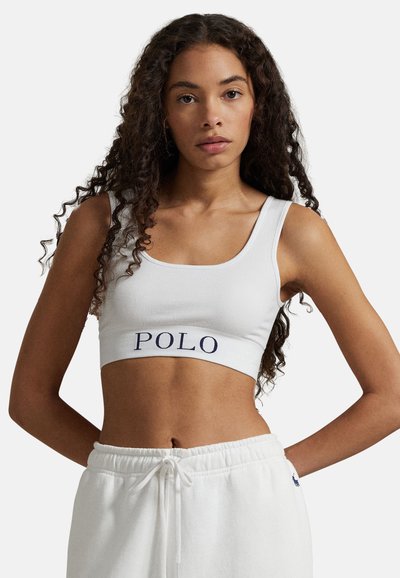 Bílý žebrovaný krátký top s výšivkou "POLO" v námořnické modři na pásku. Má široká ramínka a přiléhavý střih. Doplněn bílými kalhotami se stahovací šňůrkou.