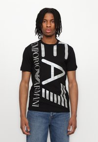 Tricou negru cu grafica mare argintie, inclusiv "EA" și "Emporio Armani," pe față. Mâneci scurte, design cu guler rotund și textură din bumbac.