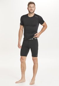 Svart atletisk tröja och shorts-set. Tröjan har en tight passform, korta ärmar, slät textur. Shortsen är kroppsnära, med en märkeslogotyp i midjan.