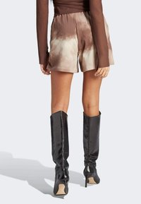 Brown tie-dye shorts with an elastic waistband, paired with sleek black knee-high boots featuring a pointed toe and stiletto heel.