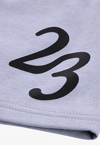 Pelēks audums ar teksturētu virsmu, uz kura redzams izteiksmīgs melns prints ar skaitli "23". Redzama dūkošana gar malu.