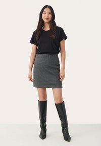Musta crew-neck t-paita, harmaa houndstooth mini-hame ja polven korkeiset mustat nahkabootsit, seisoo neutraalilla taustalla.