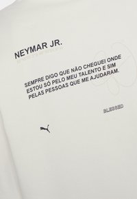 Maglietta sportiva bianca con testo nero: "NEYMAR JR." e una citazione. Include un piccolo logo Puma nero e coordinate, con "BLESSED" sotto.