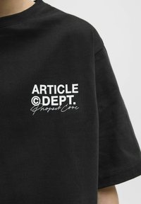 Musta puuvillane T-särk, millel on valge trükitud tekst: "ARTICLE ©DEPT. Project Core." Lühikesed varrukad ja ümar kaelus.
