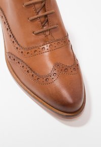 Chaussure brogue en cuir marron avec perforations détaillées et lacets, vue de face sur fond blanc.