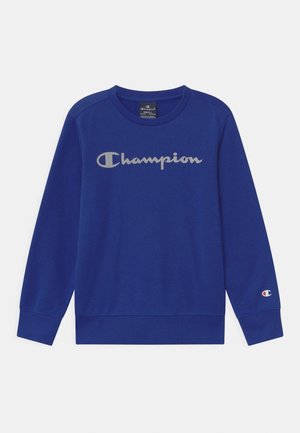 Sweat-shirt bleu à manches longues avec logo blanc Champion sur la poitrine et petit emblème Champion sur le poignet de la manche gauche.