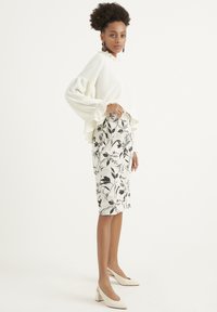 Top bianco a maniche lunghe con righe e polsini a balze, abbinato a una gonna aderente stampata floreale a lunghezza ginocchio in bianco e nero, e décolleté beige a punta.
